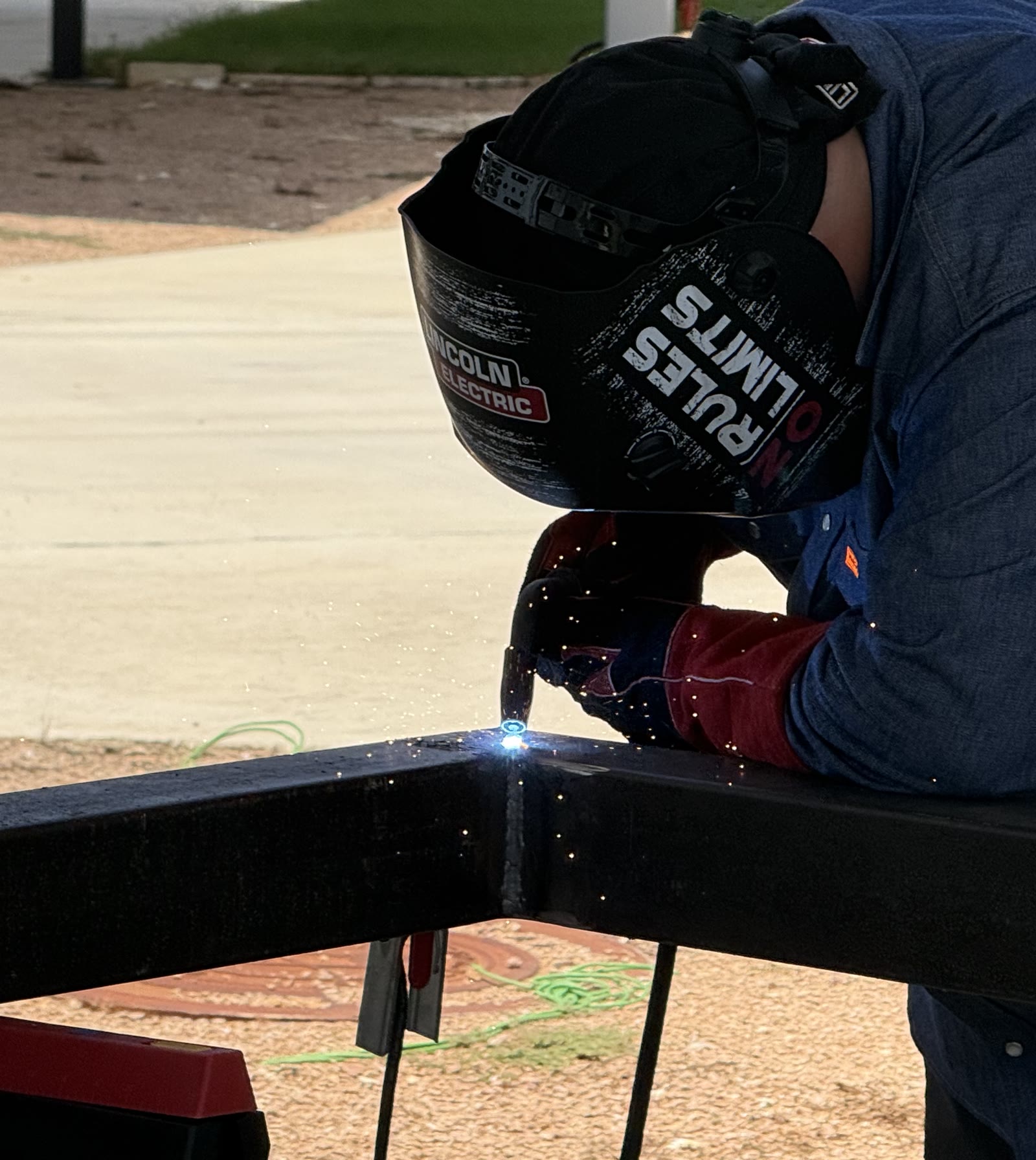 Justin Powell MIG-welding a black steel tube frame, sparks at the joint
